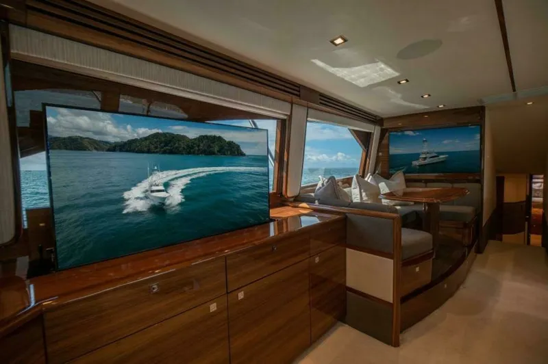 Slide: The Image of Salon with Panoramic Views and Entertainment The salon of the 2023 Viking 64 Convertible showcases luxurious seating and expansive windows offering panoramic ocean views. The high-gloss wood finish complements the modern entertainment system, creating an inviting space for relaxation and socializing - 7530839