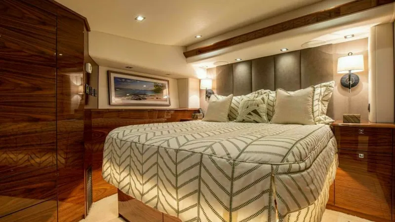 Slide: The Image of Luxurious Master Stateroom This elegant master stateroom aboard the 2023 Viking 64 Convertible features rich wood finishes and ambient lighting. The plush bedding and padded headboard create a cozy yet upscale atmosphere, while built-in storage ensures a clutter-free environment. M - 7600525