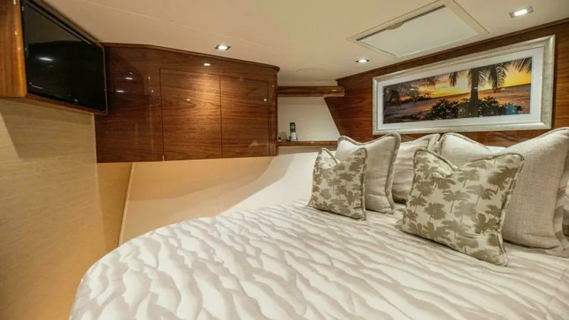 Slide: The Image of Luxurious Forward Stateroom The forward stateroom of the 2023 Viking 64 Convertible boasts elegant wood finishes and plush bedding, creating a warm and inviting atmosphere. The room features recessed lighting and a mounted television for entertainment, complemented by tasteful artwo - 7600538
