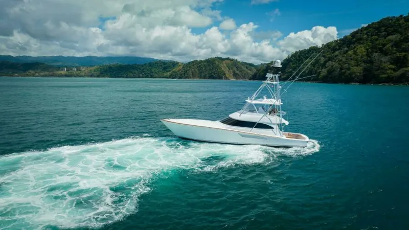 Slide: The Image of Starboard Aerial View with Wake This stunning aerial shot captures the Viking 64 Convertible 'Twin Reels' cruising powerfully through pristine waters. The sleek lines of the hull and the robust tower are highlighted against a backdrop of lush coastal scenery. The vibrant wake trailing b - 7530888