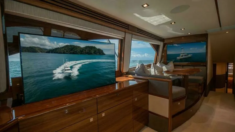 Slide: The Image of Salon with Panoramic Views and Entertainment The salon of the 2023 Viking 64 Convertible showcases luxurious seating and expansive windows offering panoramic ocean views. The high-gloss wood finish complements the modern entertainment system, creating an inviting space for relaxation and socializing - 7600521