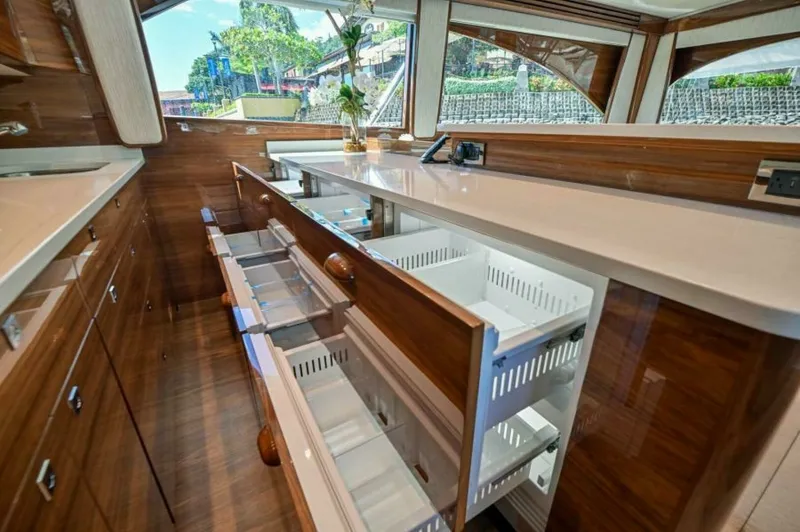 Slide: The Image of Galley with Ample Storage Drawers The galley of the 2023 Viking 64 Convertible features sleek, high-gloss wood cabinetry with multiple pull-out storage drawers, offering ample space for organizing culinary essentials. The expansive countertop provides a functional workspace, complemented - 7530836
