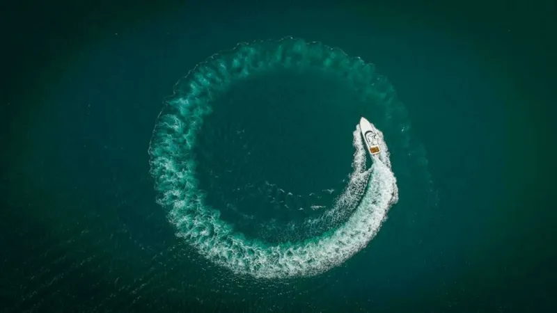 Slide: The Image of Aerial View of Twin Reels in Action This aerial shot captures the 2023 Viking 64 Convertible, Twin Reels, executing a dynamic turn on open water. The vessel demonstrates impressive agility and power, leaving a striking circular wake against the deep blue sea. The top view highlights the sle - 7530887