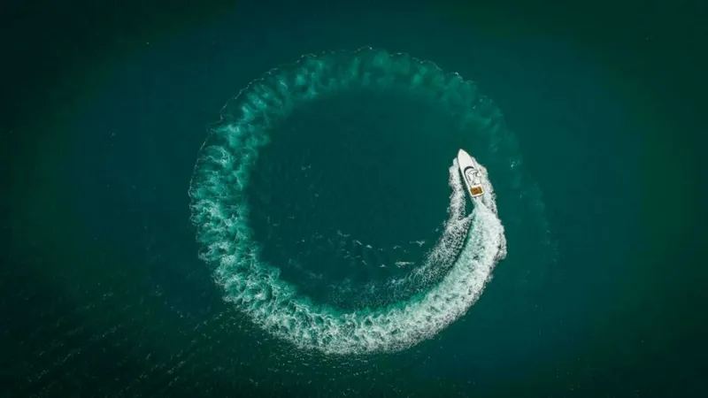 Slide: The Image of Aerial View of Twin Reels in Action This aerial shot captures the 2023 Viking 64 Convertible, Twin Reels, executing a dynamic turn on open water. The vessel demonstrates impressive agility and power, leaving a striking circular wake against the deep blue sea. The top view highlights the sle - 7600569