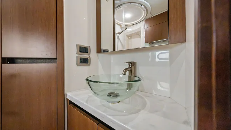 Slide: The Image of Elegant Vanity with Vessel Sink This image showcases the elegant vanity area of the 2018 Sea Ray 400 Fly, featuring a stylish glass vessel sink set atop a pristine marble countertop. The rich wood cabinetry provides ample storage, seamlessly blending with the modern fixtures for a luxur - 7762703