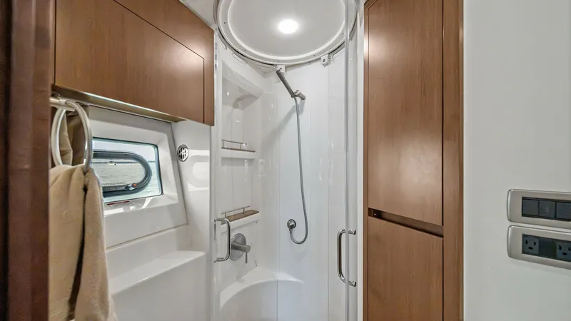 Slide: The Image of Elegant Enclosed Shower in Head This image showcases the elegant enclosed shower within the yacht's head, featuring a sleek, circular glass door design. Rich wooden cabinetry provides ample storage, complementing the modern fixtures and lighting. A small window allows natural light to e - 7762700