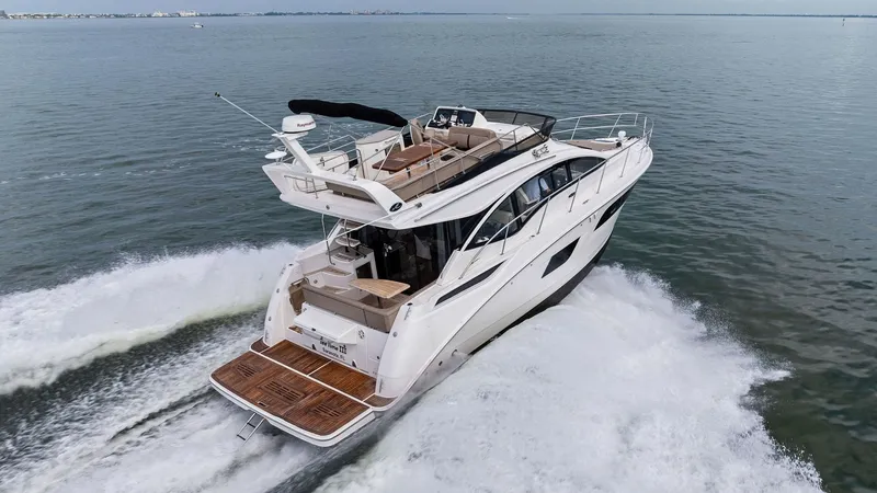 Slide: The Image of Aerial View of Flybridge and Aft Deck The 2018 Sea Ray 400 Fly, Tee Time III, is captured in motion, showcasing its elegant flybridge and spacious aft deck. The teak-lined swim platform provides a luxurious entrance, while the flybridge offers ample seating for relaxation and panoramic views. - 7762745