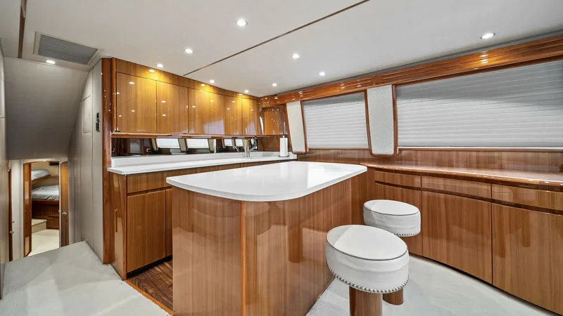 Slide: The Image of Elegant Yacht Galley with Seating The galley of the 2015 Viking 55 Convertible, Rosita, features sleek cabinetry with high-gloss wood finishes and ample storage. The pristine white countertops provide a clean and modern touch, complemented by the ambient recessed lighting above. Two comfo - 7584863