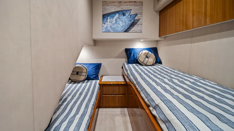 Slide: The Image of Twin Guest Stateroom with Artful Decor This cozy twin guest stateroom offers a harmonious blend of comfort and style aboard the 2015 Viking 55 Convertible. The room features two neatly arranged twin beds with nautical-themed bedding, complemented by warm wood accents. Soft lighting and a marit - 7584891