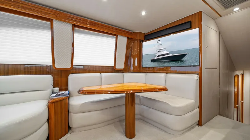 Slide: The Image of Spacious Salon with Entertainment System The salon of the 2015 Viking 55 Convertible 'Rosita' features plush, wrap-around seating upholstered in soft white fabric, creating a comfortable and inviting space. A polished wooden table serves as a central gathering point, complemented by the rich woo - 7584861