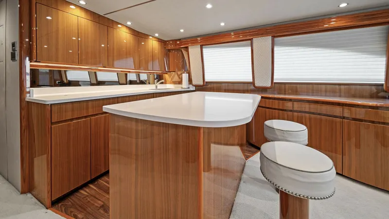 Slide: The Image of Galley with Breakfast Bar Seating This image showcases the elegant galley of the 2015 Viking 55 Convertible, featuring high-gloss wooden cabinetry and a pristine white countertop. The spacious breakfast bar is complemented by stylish stools, making it an ideal spot for casual dining. Ampl - 7584872