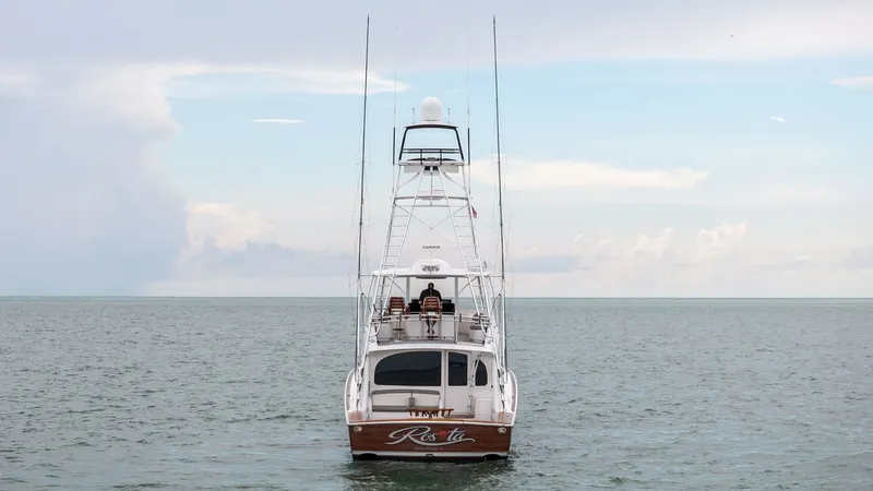 Slide: The Image of Aft View with Tower and Nameplate The 2015 Viking 55 Convertible 'Rosita' is prominently displayed from the aft, showcasing its sleek lines and robust fishing tower. The nameplate is elegantly positioned above the transom, adding a touch of personalization. The open deck design highlights - 7584920