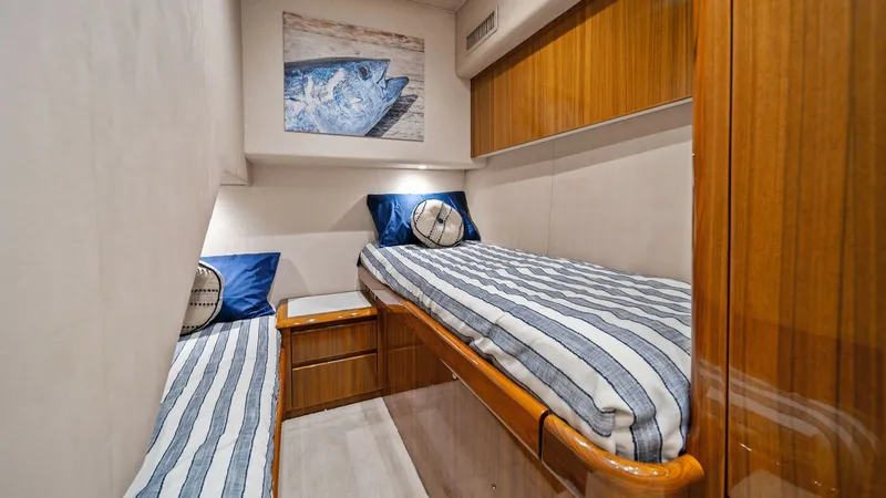Slide: The Image of Guest Stateroom with Twin Berths This cozy guest stateroom features twin berths adorned with striped bedding and nautical-themed cushions. The warm wood cabinetry provides ample storage, complemented by soft overhead lighting that enhances the inviting atmosphere. A piece of marine artwo - 7584890
