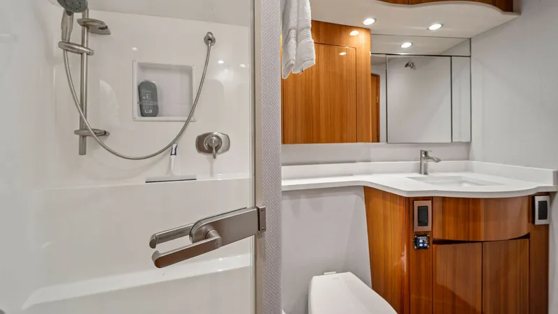 Slide: The Image of Luxurious Ensuite Bathroom This elegant ensuite bathroom aboard the Viking 55 Convertible features a sleek, modern shower with chrome fixtures and a built-in shelf. The vanity is beautifully crafted with rich wood cabinetry, complemented by a pristine white countertop and undermoun - 7584883