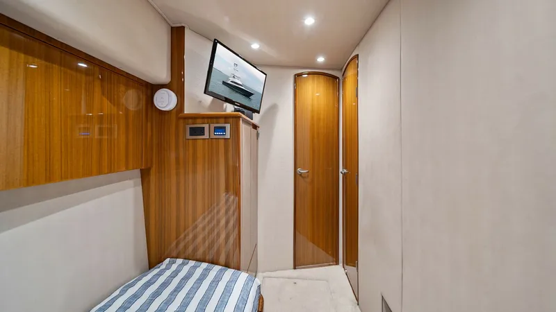 Slide: The Image of Guest Cabin with Ensuite Access This inviting guest cabin on the Viking 55 Convertible features a cozy berth with elegant striped bedding. The room boasts warm wood finishes and built-in storage, complementing the modern entertainment system. Recessed lighting and ensuite access provide - 7584892