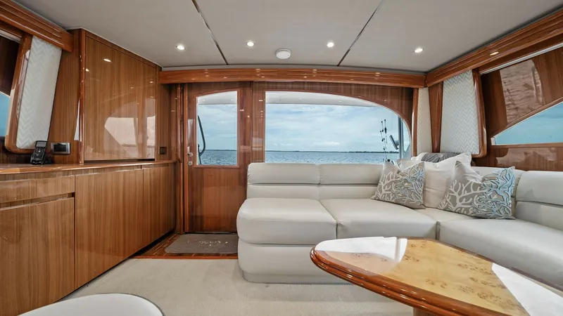 Slide: The Image of Spacious Salon with Ocean Views The salon of the 2015 Viking 55 Convertible boasts a luxurious and inviting atmosphere, featuring a plush L-shaped sofa and high-gloss wood finishes. Large windows provide stunning ocean views, enhancing the bright and open feel of the space. Elegant ligh - 7584873