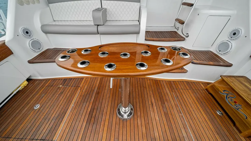 Slide: The Image of Cockpit with Teak Flooring and Seating The cockpit of the 2015 Viking 55 Convertible, Rosita, showcases elegant teak flooring complemented by a sleek, varnished table with multiple cup holders. The built-in cushioned bench provides comfortable seating, while the surrounding steps and storage a - 7584858