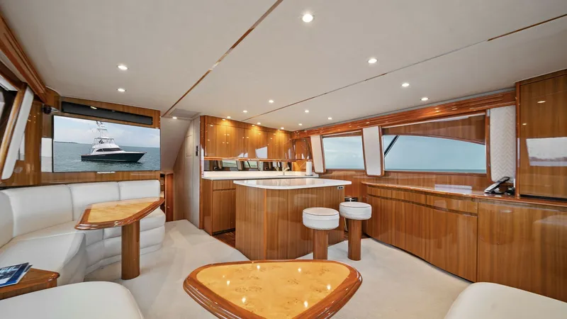 Slide: The Image of Spacious Salon with Elegant Seating The salon of the 2015 Viking 55 Convertible, 'Rosita,' showcases luxurious high-gloss wooden finishes and plush seating arrangements. Large windows provide abundant natural light and stunning ocean views, enhancing the open and inviting atmosphere. The ce - 7584880