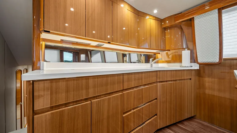 Slide: The Image of Galley with High-Gloss Cabinetry The galley of the 2015 Viking 55 Convertible features luxurious high-gloss wooden cabinetry, providing ample storage space. A pristine white countertop complements the sleek design, while recessed lighting adds a touch of elegance. The modern faucet and i - 7584869