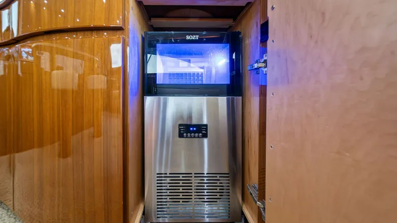 Slide: The Image of Built-In Ice Maker Compartment This image showcases the built-in ice maker compartment on the Viking 55 Convertible 'Hot Spot.' The sleek stainless steel appliance is neatly integrated within a polished wooden cabinet, adding a touch of luxury to the interior. The ambient lighting and - 7962068