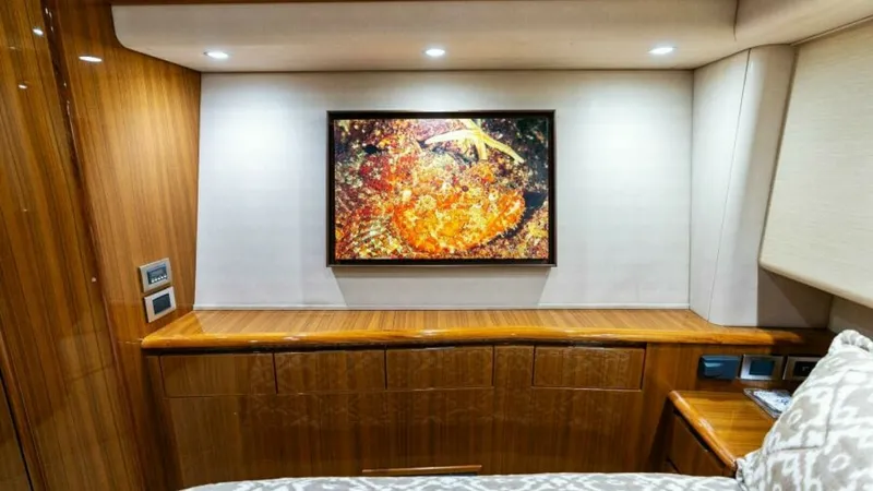 Slide: The Image of Guest Stateroom with Art Decor The guest stateroom features elegant wood cabinetry with a glossy finish, creating a warm and inviting atmosphere. A vibrant artwork serves as a focal point, complemented by recessed lighting that enhances the room's cozy ambiance. The soft, patterned bed - 7594247