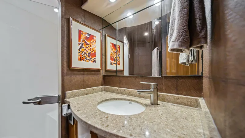 Slide: The Image of Elegant Guest Head with Vanity This stylish guest head on the Viking 55 Convertible features a sleek vanity with a polished stone countertop and modern fixtures. The mirrored wall enhances the space, reflecting the warm tones of the woodwork and chic wall art. Recessed lighting adds a - 7962071