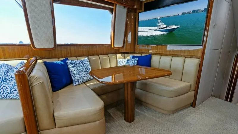 Slide: The Image of Salon Dining Area with Entertainment The salon of the 2013 Viking 55 Convertible features a cozy dining area with plush L-shaped seating and a polished wooden table, perfect for casual meals or gatherings. Large windows allow natural light to fill the space, enhancing the warm wood finishes. - 7594242