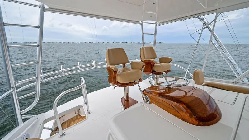 Slide: The Image of Flybridge Helm Station with Seating Experience commanding views from the flybridge helm station of the 2013 Viking 55 Convertible. The area features two luxurious captain's chairs and a beautifully crafted wooden helm console, offering both comfort and style. With open views of the surround - 7962095