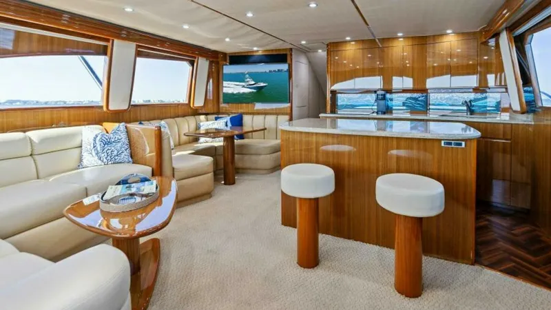 Slide: The Image of Spacious Interior Salon with Bar This elegant interior salon on the 2013 Viking 55 Convertible 'Hot Spot' features plush L-shaped seating and a beautifully crafted teak finish. The open layout showcases a stylish bar area with two stools, perfect for entertaining guests. Large windows fl - 7594232