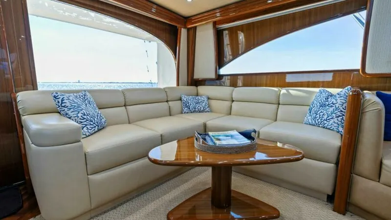 Slide: The Image of Luxurious Salon Seating Area The salon of the Viking 55 Convertible features an elegant L-shaped leather sofa, complemented by patterned throw pillows for added comfort. A polished wood coffee table serves as the centerpiece, enhancing the sophisticated ambiance. Large windows provid - 7594234