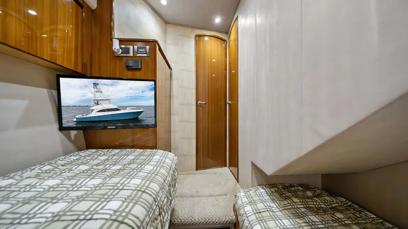 Slide: The Image of Guest Cabin with Twin Berths This inviting guest cabin features twin berths with stylish plaid bedding, offering a cozy retreat aboard the Viking 55 Convertible. The warm wood finishes and soft lighting create an elegant atmosphere, while the flat-screen TV adds a touch of modern con - 7962083
