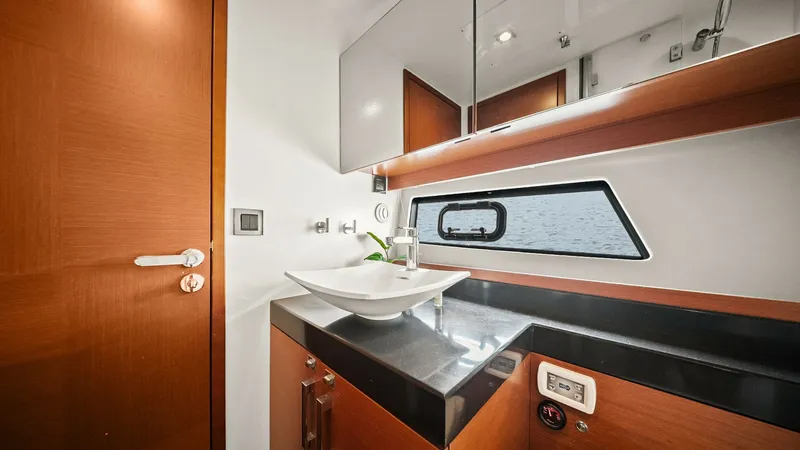 Slide: The Image of Modern Yacht Bathroom with Elegant Vanity This stylish bathroom aboard the 2015 Prestige 500 Fly showcases a sleek vanity with a vessel sink and polished fixtures. The warm wood cabinetry complements the black countertop, creating a sophisticated ambiance. A mirrored cabinet above offers ample st - 7603813
