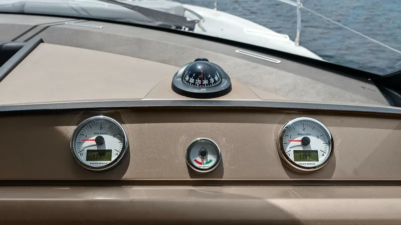 Slide: The Image of Helm Console with Gauges and Compass The helm console of the Prestige 500 Fly features a sleek design with essential navigation instruments. Prominently displayed are two clear analog gauges and a central compass, providing precise navigation and engine information. This setup ensures a seam - 7603796