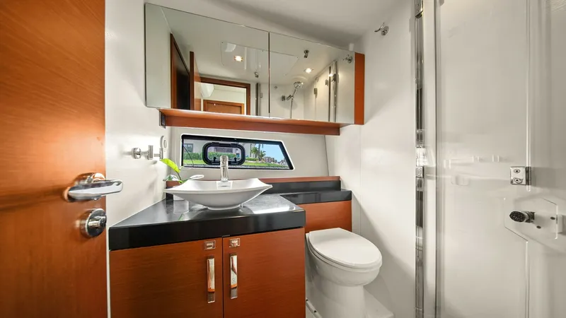 Slide: The Image of Contemporary Yacht Bathroom This elegant bathroom on the Prestige 500 Fly features modern finishes and a sleek design. The vessel sink sits atop a dark countertop, complemented by rich wood cabinetry and a mirrored storage unit. Natural light floods in through the window, enhancing - 7603818
