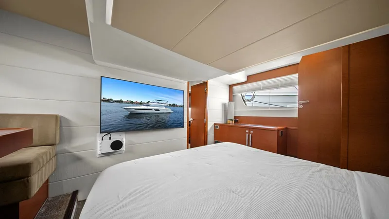 Slide: The Image of Master Stateroom with Entertainment System The master stateroom features a plush bed with crisp, white linens and warm wood finishes that create a cozy yet elegant atmosphere. A large flat-screen TV is mounted on the wall for entertainment, complemented by sleek cabinetry offering ample storage sp - 7603803