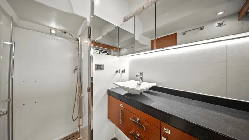 Slide: The Image of Elegant Bathroom with Modern Vanity This stylish bathroom aboard the 2015 Prestige 500 Fly showcases a sleek design with a contemporary vanity featuring a vessel sink and rich wood cabinetry. The walk-in shower is adorned with a teak grate floor, adding a touch of luxury. Ample mirrored sto - 7603805