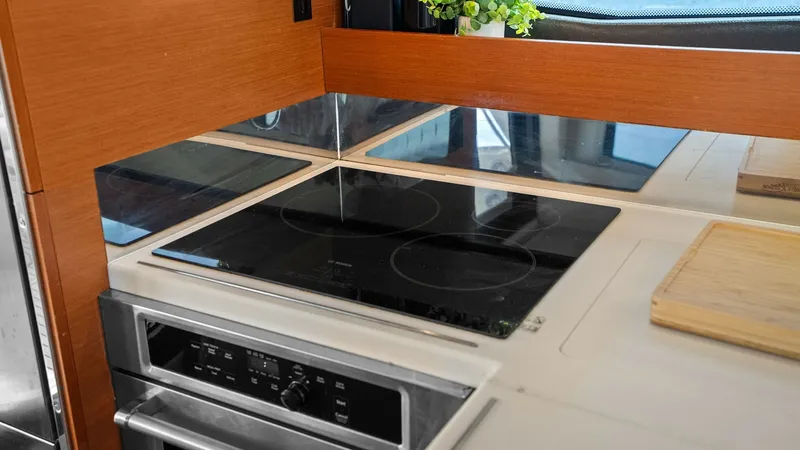 Slide: The Image of Galley with Modern Cooktop The galley on the Prestige 500 Fly showcases a sleek, modern cooktop set within a polished countertop. Warm wood cabinetry and stainless steel appliances provide a sophisticated yet functional cooking space. Natural light flows through the nearby window, - 7603779