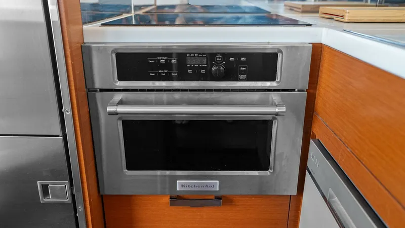 Slide: The Image of Galley with Modern Appliances This image shows the well-appointed galley of the 2015 Prestige 500 Fly, featuring a sleek stainless steel oven by KitchenAid. The warm wooden cabinetry contrasts beautifully with the modern appliances, while the induction cooktop offers efficient cooking - 7603780