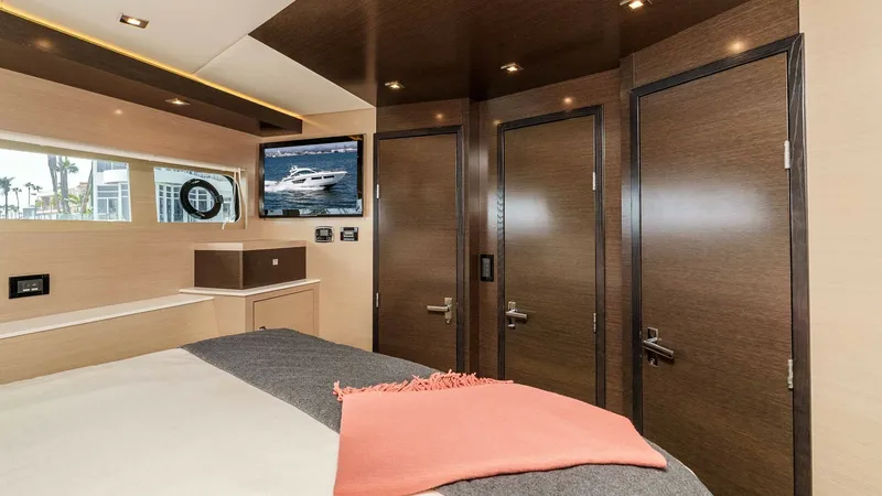 Slide: The Image of 2017 Cruisers 60 Cantius 'Rising Star' - Forward VIP Stateroom with Corridor, Closet, and Ensuite Access. The forward VIP stateroom on the 2017 Cruisers 60 Cantius 'Rising Star' showcases a luxurious and spacious design. It features modern wood finishes, ample natural light through a side window, and a wall-mounted TV for entertainment. The ensuite access enh - 7603863