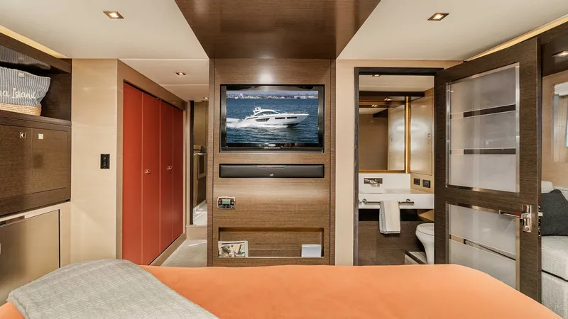 Slide: The Image of 2017 Cruisers 60 Cantius 'Rising Star' - Master Stateroom Entry & Ensuite The master stateroom of the 2017 Cruisers 60 Cantius 'Rising Star' showcases luxurious design with a spacious layout. It features a plush bed with elegant bedding, warm wood finishes, and a flat-screen TV for entertainment. The ensuite bathroom, visible t - 7603856