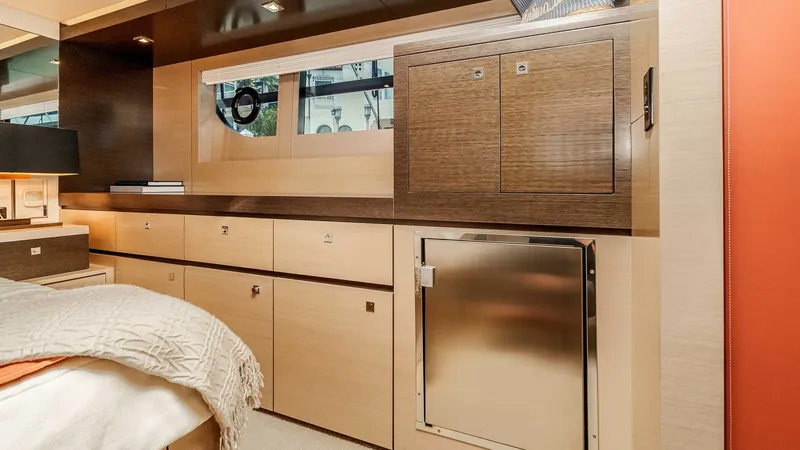 Slide: The Image of 2017 Cruisers 60 Cantius 'Rising Star' - Master Stateroom Showcases Rich Wood Cabinetry & Stainless-Steel Mini-Fridge for a Stylish, Sophisticated Finish. The master stateroom features elegant cabinetry with ample storage, blending light and dark wood finishes for a sophisticated look. A stainless steel mini-fridge is seamlessly integrated, providing convenience and style. Large windows invite natural light - 7603859