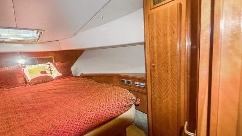 Slide: The Image of Forward Stateroom with Queen Berth The forward stateroom of the 2005 Meridian 540 Pilothouse features a luxurious queen-sized berth adorned with rich, patterned bedding. Warm wood cabinetry and paneling create an inviting, elegant atmosphere, while the overhead hatch provides natural light - 7721607