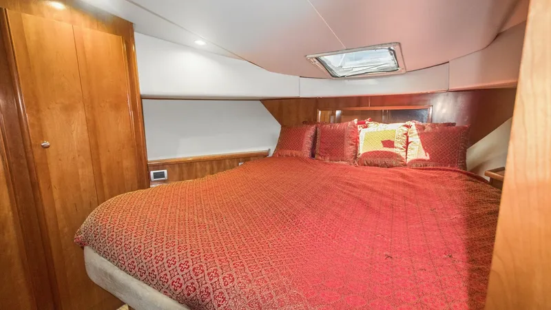 Slide: The Image of Forward Stateroom with Queen Berth This inviting forward stateroom features a luxurious queen-size berth adorned with plush red bedding, creating a cozy retreat. The space is accented by warm wood cabinetry and soft overhead lighting, enhancing the elegant ambiance. A skylight above allows - 7721608