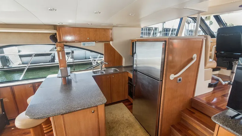 Slide: The Image of Galley and Helm Station View The image showcases the galley area of the 2005 Meridian 540 Pilothouse, featuring a sleek countertop with integrated appliances. Rich wooden cabinetry complements the space, providing ample storage and a warm ambiance. Adjacent to the galley, the helm st - 7721599