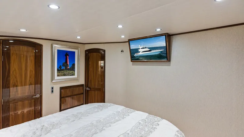 Slide: The Image of Guest Stateroom with TV and Art The guest stateroom features a comfortable bed with elegant bedding, surrounded by rich wood finishes. A wall-mounted TV offers entertainment, while tasteful artwork adds a touch of sophistication. Recessed lighting enhances the cozy atmosphere, making th - 7751239
