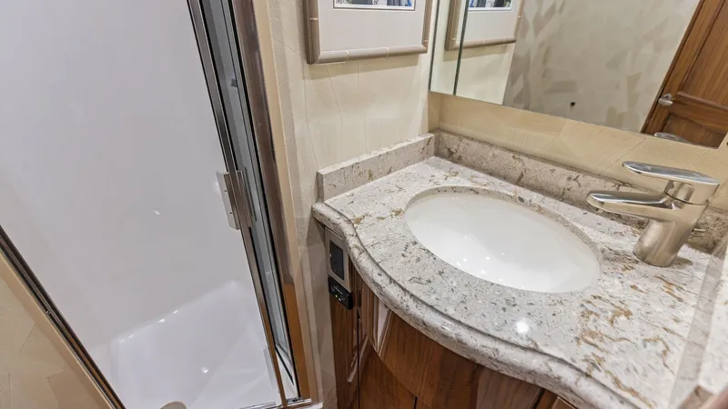 Slide: The Image of Luxurious Bathroom Vanity and Shower This elegant bathroom aboard the Viking 62 Enclosed Bridge features a sleek, granite countertop with an undermount sink and modern fixtures. The compact yet functional shower is enclosed with a clear door, providing a comfortable space for freshening up. - 7751262