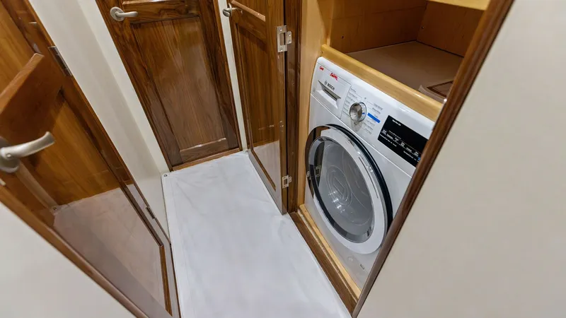 Slide: The Image of Laundry Area with Washer This image showcases the compact laundry area on the Viking 62 Enclosed Bridge, featuring a state-of-the-art washer neatly integrated into the cabinetry. The space is efficiently designed with rich wood finishes and ample shelving, providing both function - 7751232
