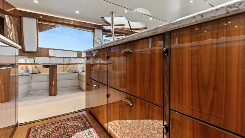 Slide: The Image of Galley and Salon View This image showcases the elegant galley of the 2018 Viking 62 Enclosed Bridge, complete with sleek wooden cabinetry and polished countertops. The space seamlessly flows into the salon, offering a cozy seating area with plush cushions and expansive windows - 7751227