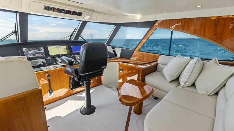 Slide: The Image of Enclosed Bridge Helm and Lounge Area The enclosed bridge of the 2018 Viking 62 showcases a sophisticated helm station equipped with advanced navigation systems. Luxurious leather seating provides comfort, complemented by rich wood finishes and expansive windows offering panoramic ocean views - 7751272