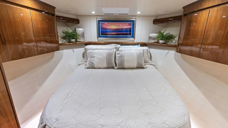Slide: The Image of Luxurious Forward Stateroom Interior This elegant forward stateroom on the Viking 62 Enclosed Bridge showcases a plush centerline queen berth, framed by high-gloss wood cabinetry. Soft ambient lighting and a large overhead hatch enhance the serene atmosphere, complemented by tasteful decor a - 7751249